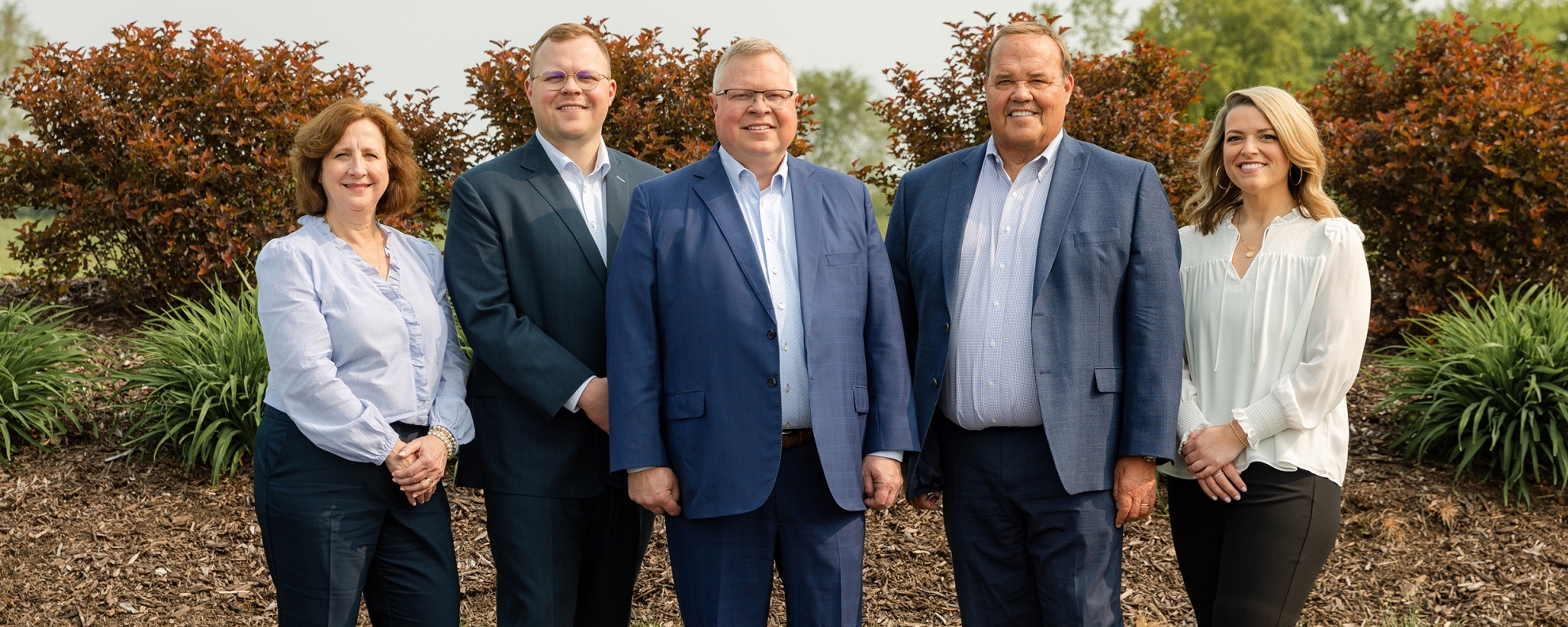 Stifel | Schluckebier Hood Wealth Management Group team photo, the image was taken outside in front of dark red bushes